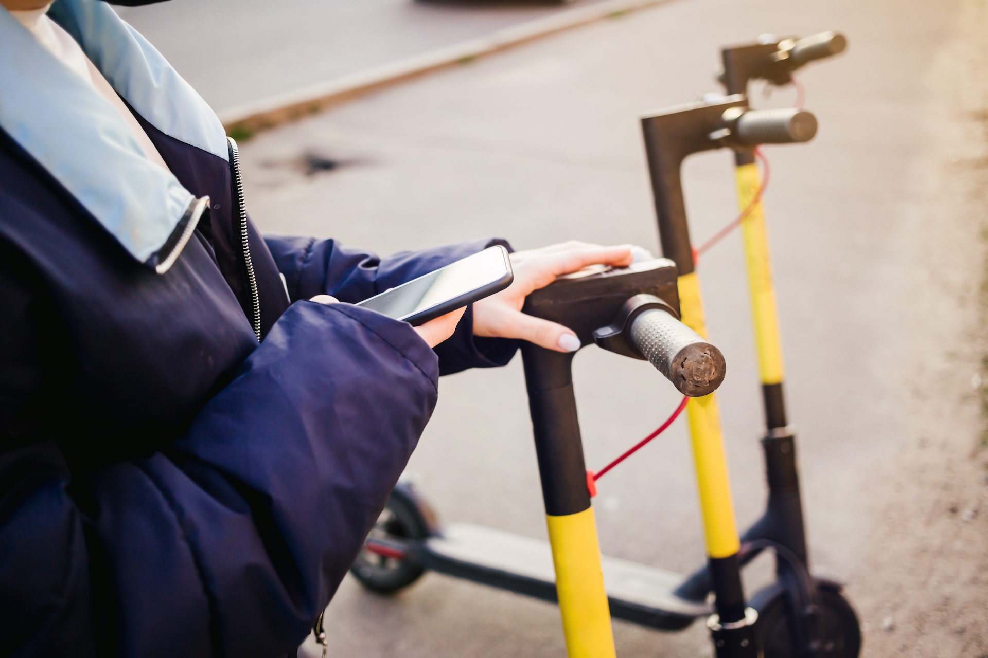 A person holding a phone, reaching for an electric scooter.